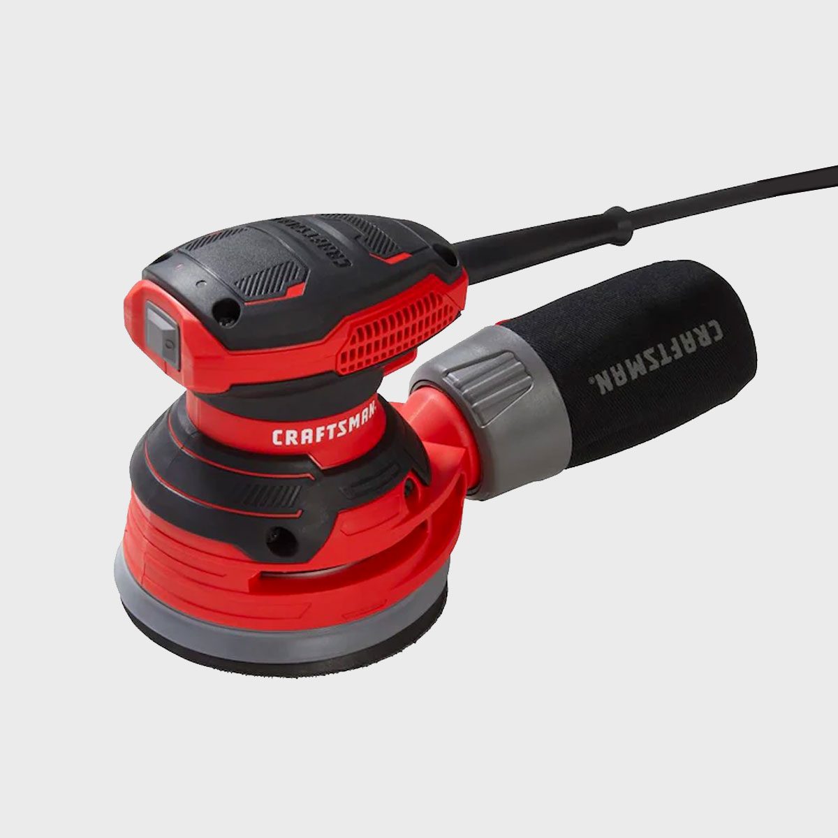 A red and black orbital sander is positioned horizontally, featuring a circular sanding pad, a power cord, and a textured grip for user control.