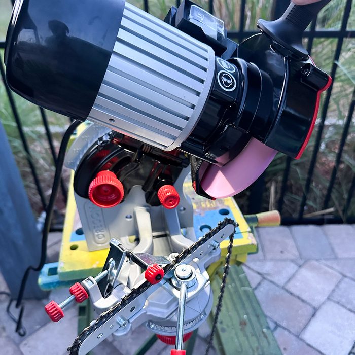 A power tool with a large blade is mounted on a table, poised for action, amidst a background of greenery and stone flooring.
