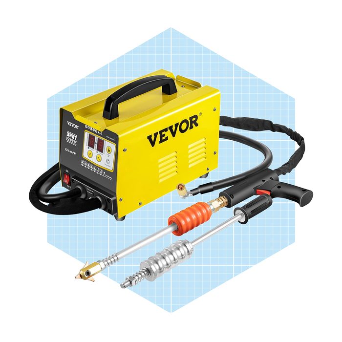 A yellow welding machine sits with a connected welding torch and hose, positioned against a light blue grid background, indicating a workshop or technical setting.