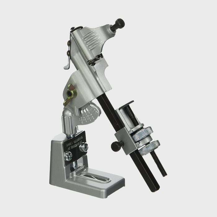 A silver mechanical device sits on a base, holding a black rod in place, likely used for precision work or crafting in a workshop setting.