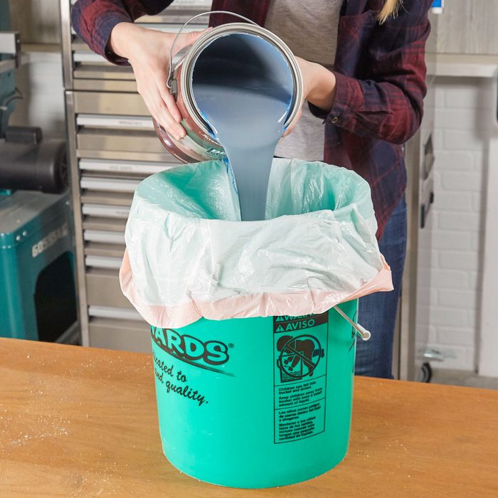 person pouring paint into a 5 gallon bucket that is lined with a garbage bag
