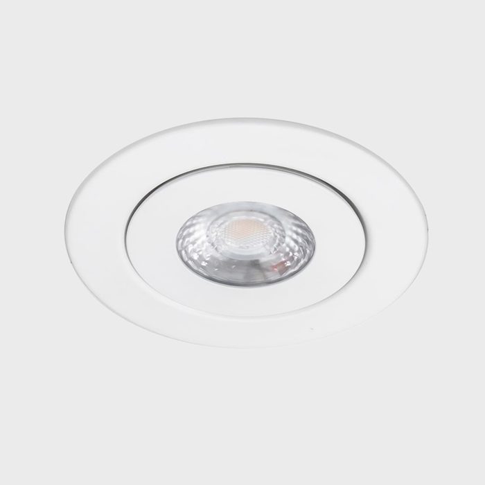 A circular recessed light fixture is mounted in a white ceiling, illuminating the area with a focused beam. The design is sleek and modern.