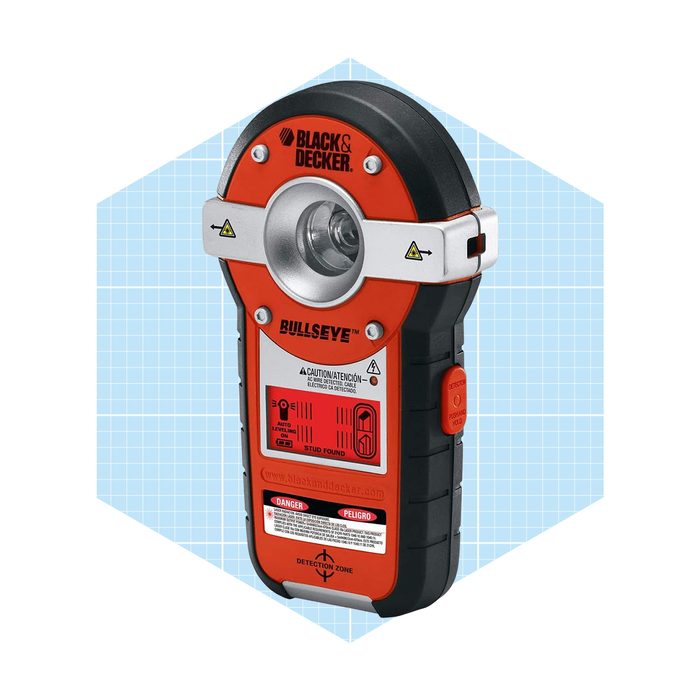 A handheld detection tool identifies studs behind walls, featuring a circular light and various buttons. It has a black and orange design against a light blue background.