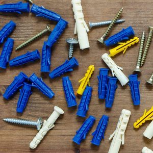 Plastic anchors and screws scatter across a wooden surface, suggesting preparation for installation or assembly tasks. Various colors and sizes provide options for different applications.