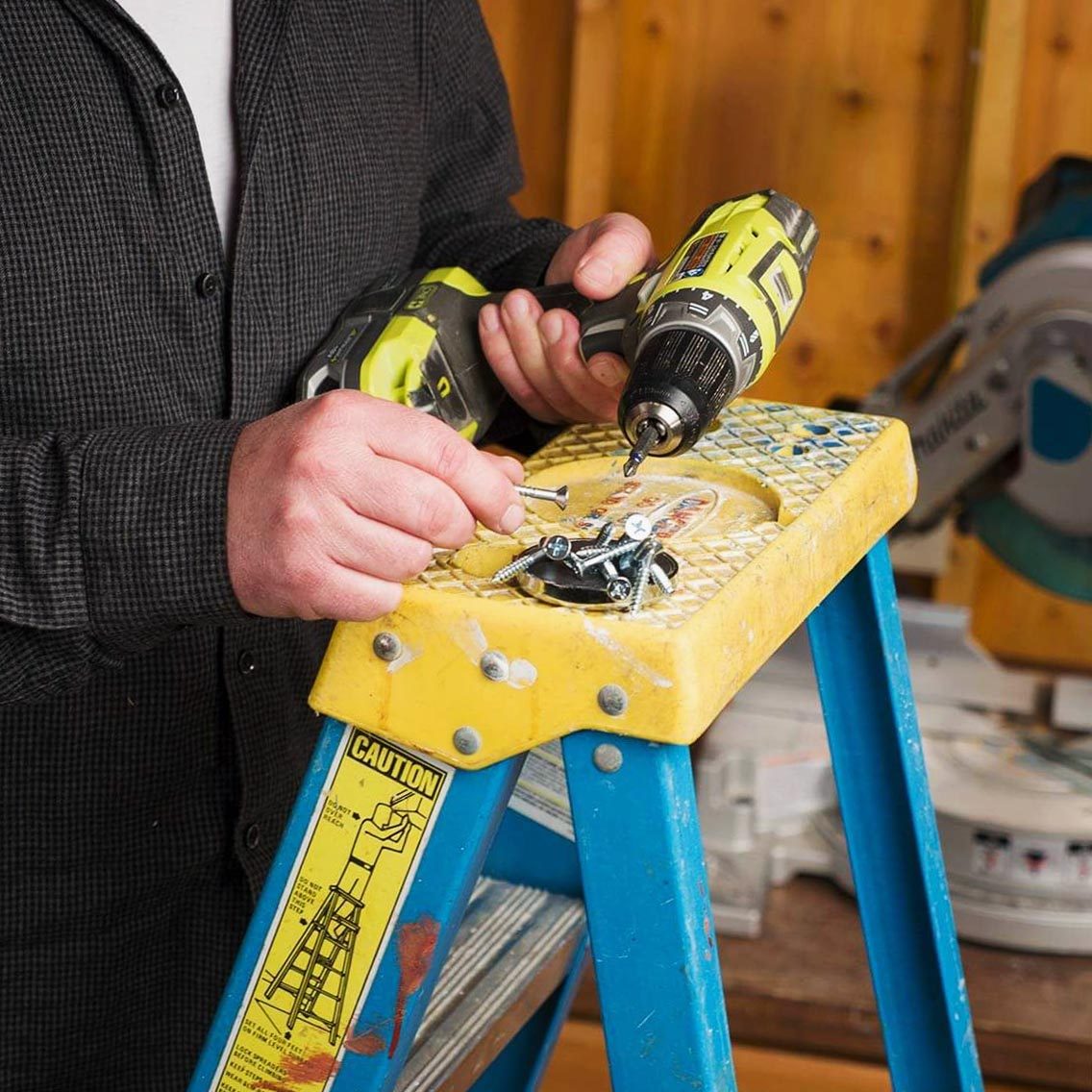 a pile of screws on the top of a ladder, hands holding a drill next to it