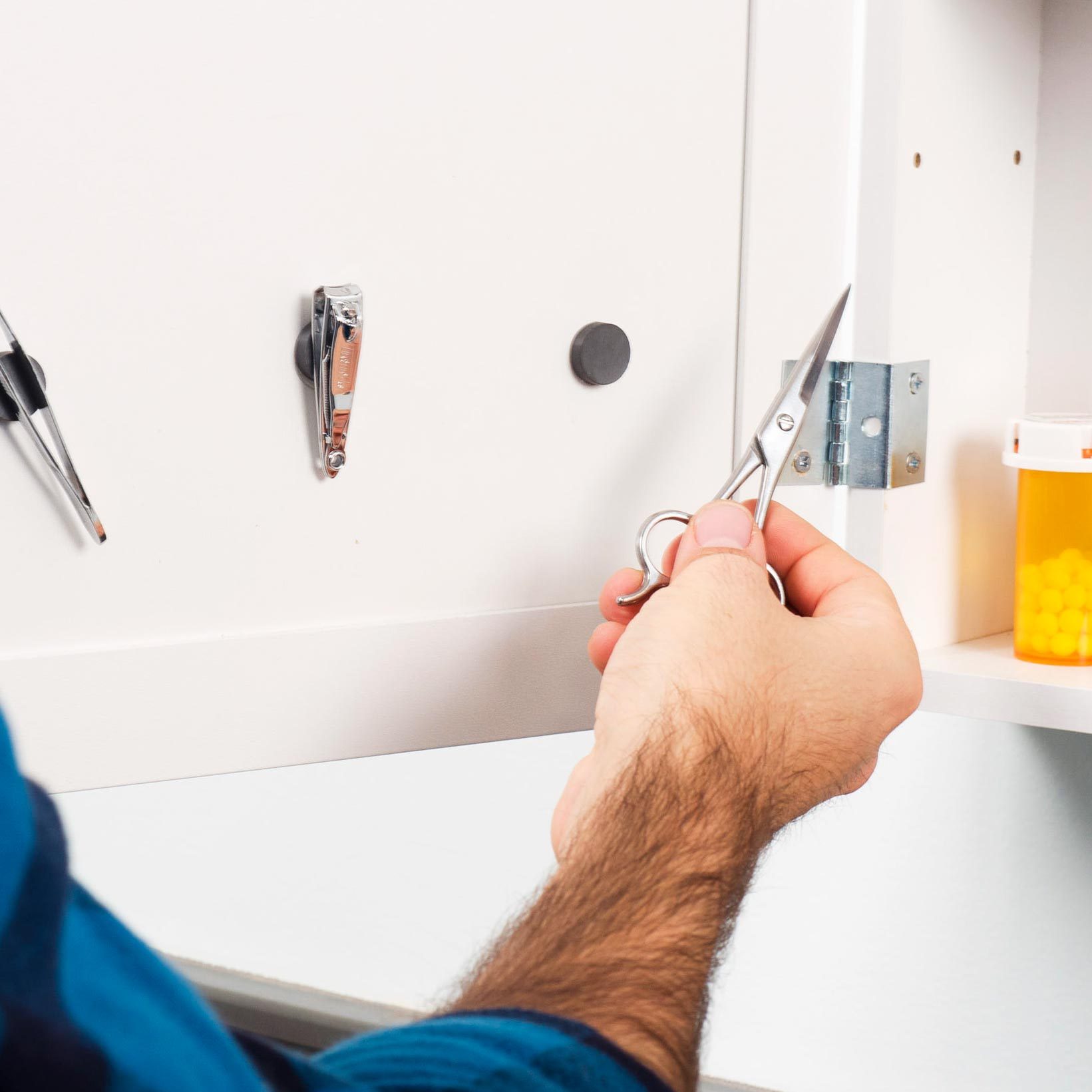 a hand putting a small pair of scissors on a magnet that is attached to the inside of a bathroom cabinet