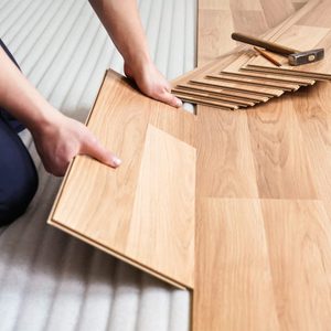 A person is laying wooden flooring tiles on a soft underlayment in preparation for installation, with tools nearby for securing the pieces.