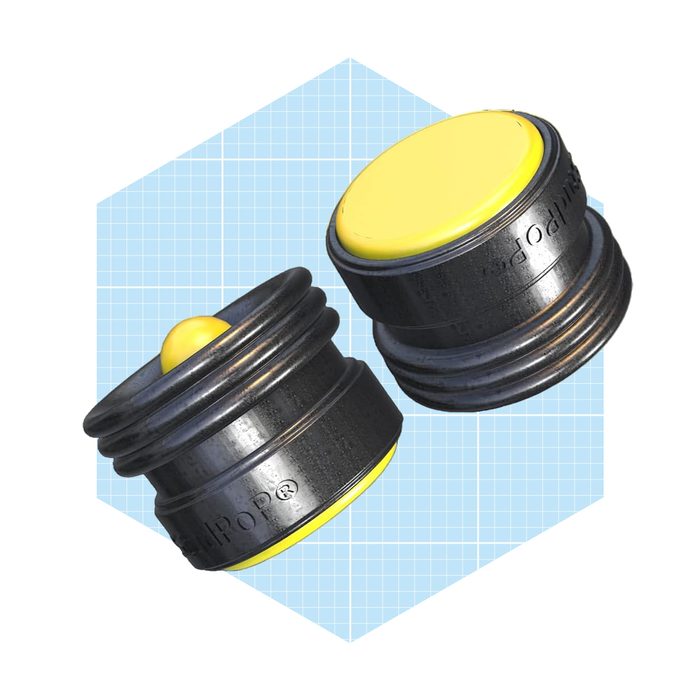 Two round, black rubber stoppers with yellow tops sit upright on a light blue geometric background, showcasing their contrasting colors and shapes.