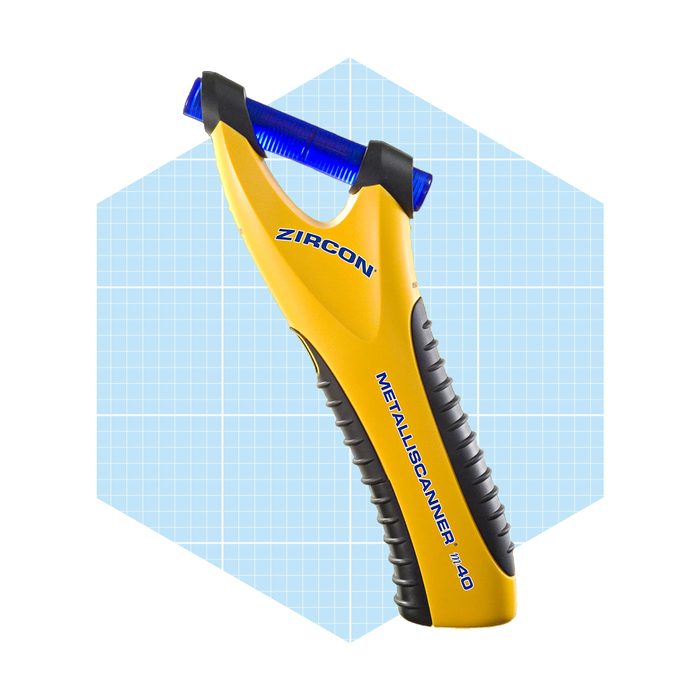 A yellow metal scanner is held upright, scanning for metal objects, set against a light blue grid-patterned background.