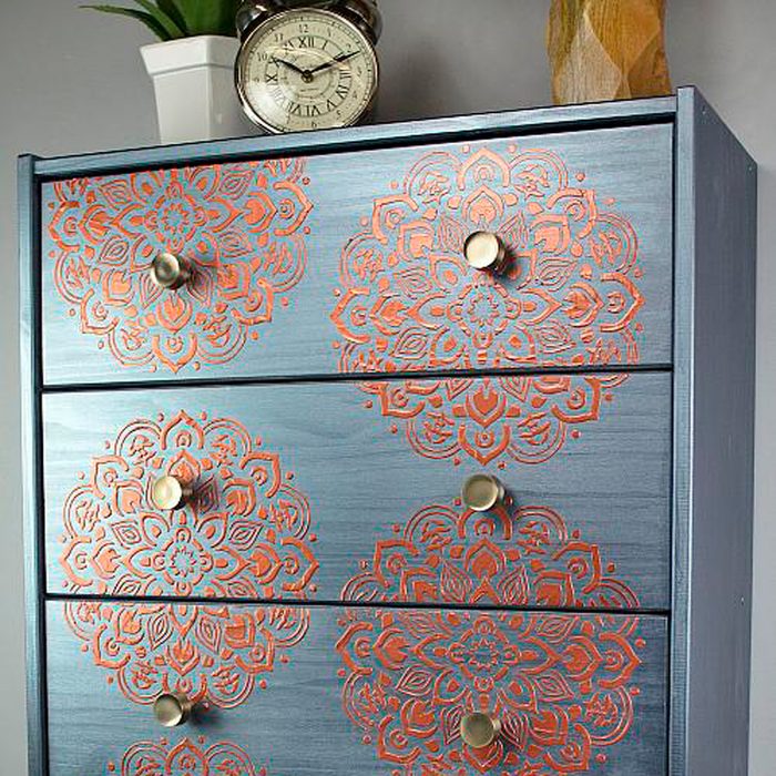 A blue dresser features intricate orange mandala designs on its front. It