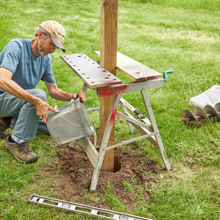 putting a fence stake into the ground with concrete around the base