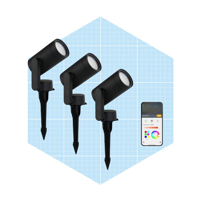 Three black spotlight fixtures are placed upright, projecting light, alongside a smartphone displaying lighting control options, set against a light blue grid background.