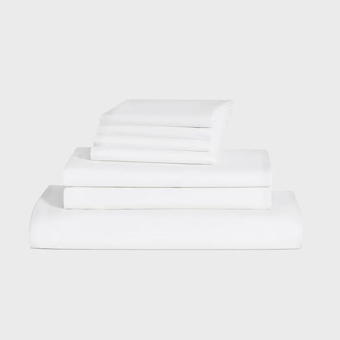 Stacked white bed sheets and pillowcases are neatly arranged in four layers, showcasing their smooth texture against a plain, light background.