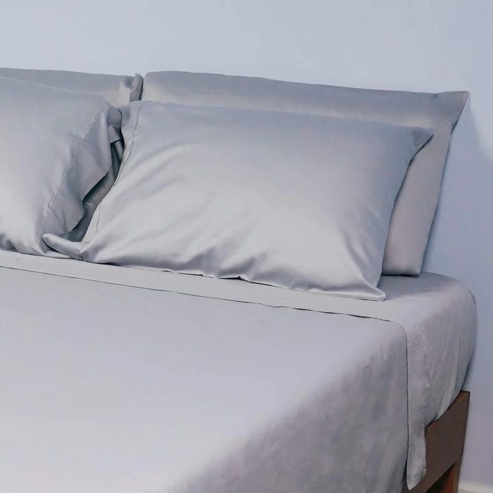 A neatly made bed features two soft, gray pillows resting against a plain wall, creating a calm and inviting atmosphere.
