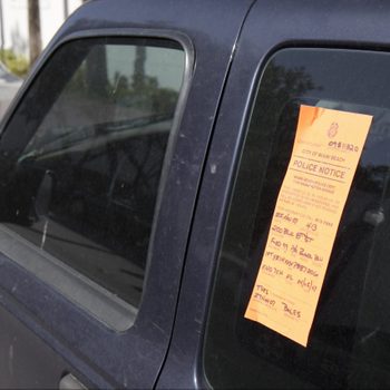 An orange police notice is affixed to the dark window of a vehicle, indicating a violation of parking regulations in Miami Beach.