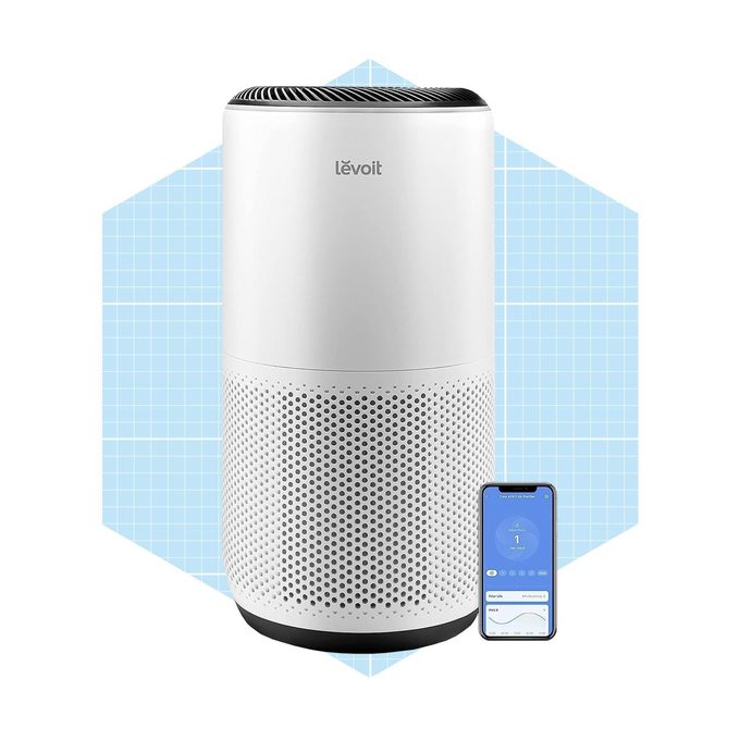A white air purifier stands vertically, displaying a sleek design. A smartphone beside it shows an app interface for monitoring air quality.
