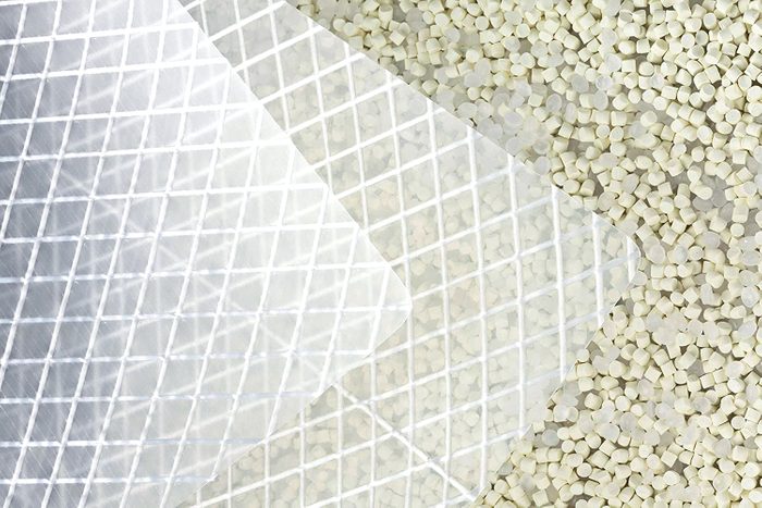 A transparent plastic sheet with a grid pattern overlaps small round pellets, all situated on a light surface, suggesting a packaging or crafting context.