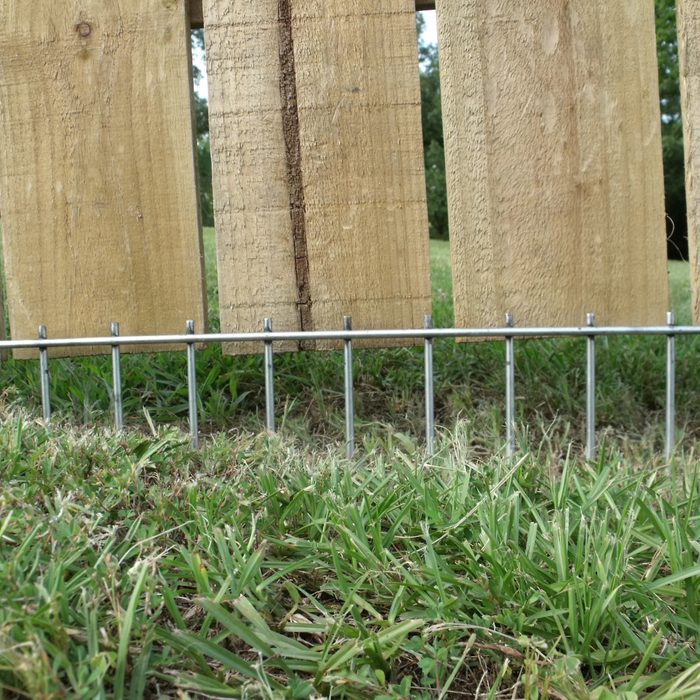 Wooden panels lean against each other, while a row of metal stakes secures them into a grassy field under an open sky.