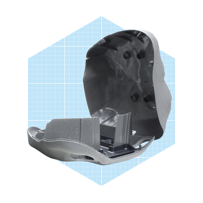 A gray plastic object is split in half, revealing an interior structure with holes, set against a light blue graph paper background.