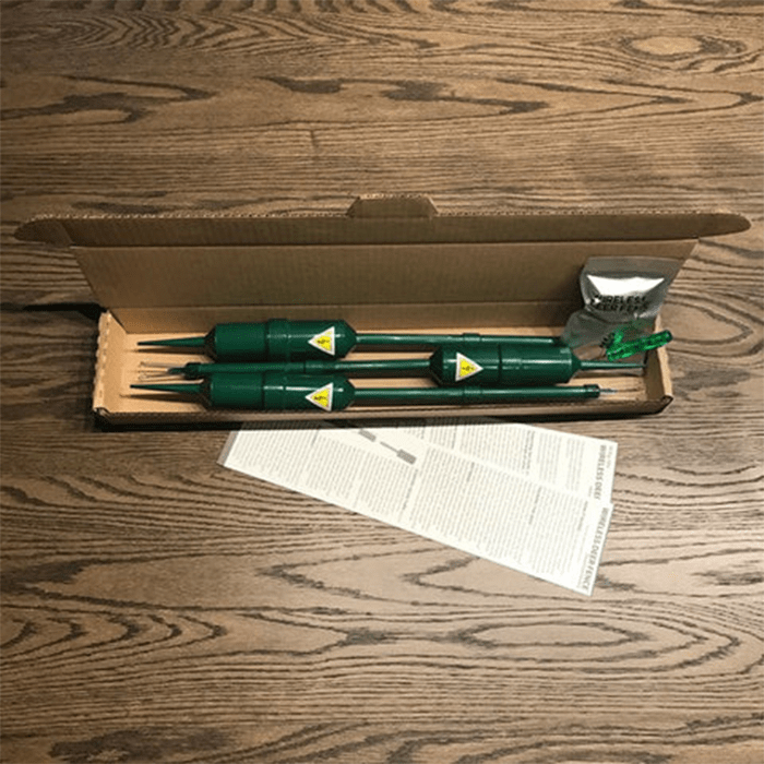 Green gardening tools with pointed ends are arranged in a cardboard box, alongside instructions and a small package, on a wooden surface.