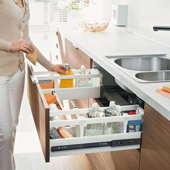 A person retrieves a snack while exploring a well-organized kitchen drawer filled with various food items and drinks, set within a modern kitchen.