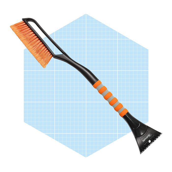 A black and orange snow brush rests against a light blue grid background, designed for scraping snow and ice off car windshields.