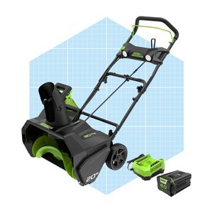 A black and green snow blower stands upright, with a chute pointing forward. Two detachable batteries are positioned beside it on a light blue grid background.