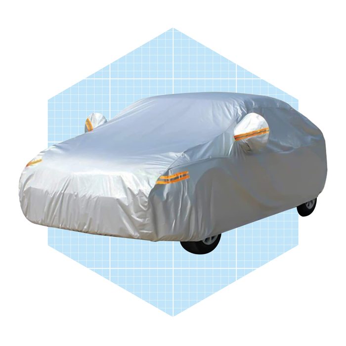 A car is covered with a silver protective cover, highlighting its shape, on a light blue grid-patterned background.