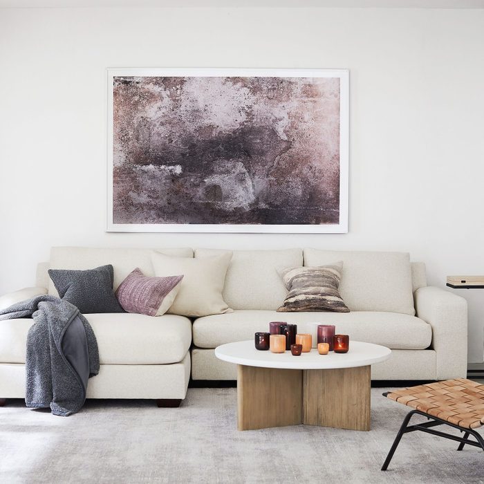 A sofa with decorative pillows and a blanket displays a centerpiece of colorful candles on a circular table, set against a minimalist wall with artwork.