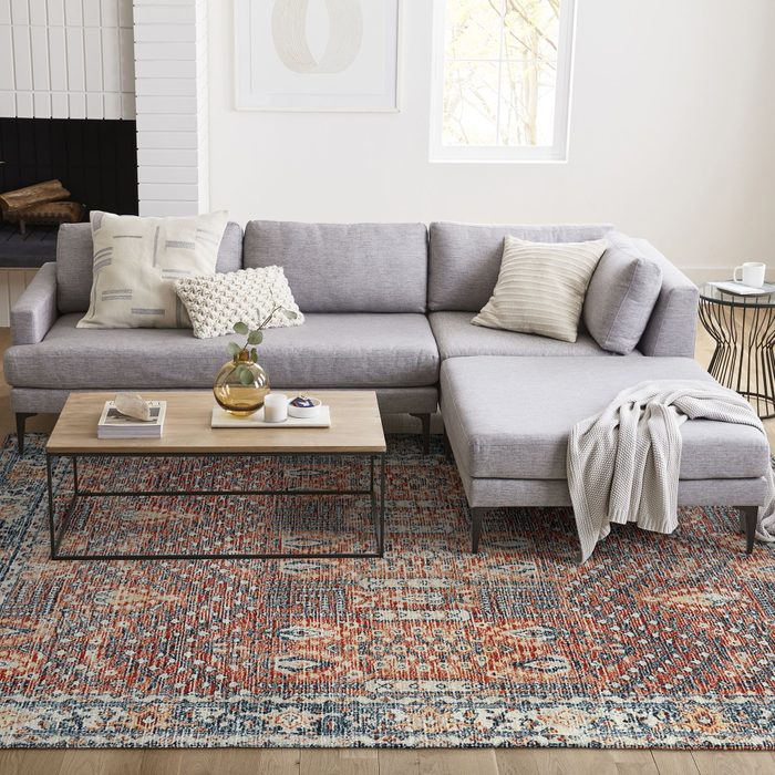 A gray sectional sofa with decorative pillows is positioned alongside a wooden coffee table. A colorful rug and a cozy throw blanket enhance the inviting living space.