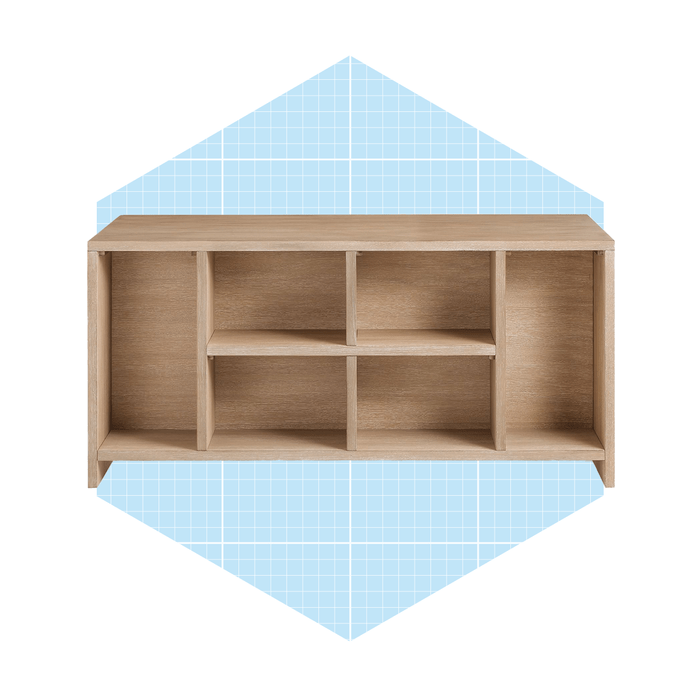 A wooden shelving unit features multiple compartments, positioned against a light blue grid background, suggesting a modern design aesthetic suitable for storage or display.