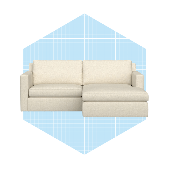 A light-colored sectional sofa rests on a solid background, featuring a hexagonal shape filled with a blue grid pattern, suggesting a modern design context.