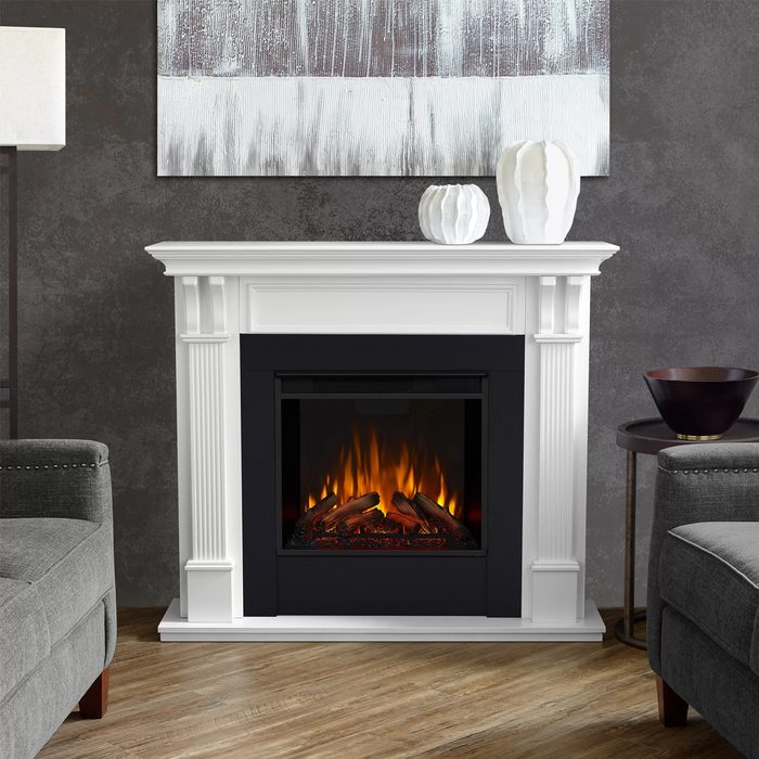 A white fireplace emits a warm glow, surrounded by modern furnishings in a stylish room with textured walls and decorative items on the mantel.
