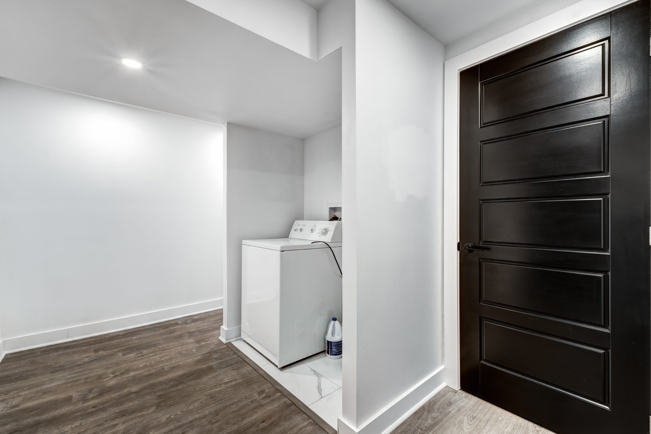 a washing machine in a refinished basement with bright white walls and a wood floor