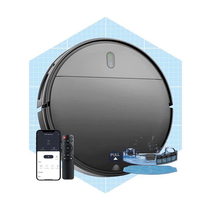 A round, black robotic vacuum is displayed alongside a smartphone and remote, suggesting remote cleaning control in a bright, grid-patterned background.