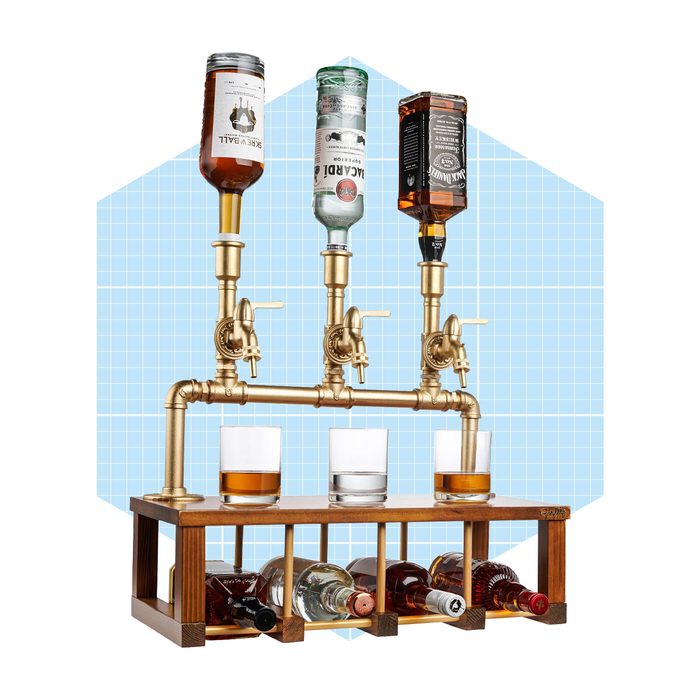 A stylish beverage dispenser features three bottle holders pouring into glasses, with a wooden base displaying additional liquor bottles, set against a blue background.