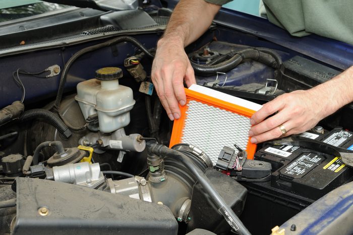 A person installs an orange-framed air filter in a vehicle