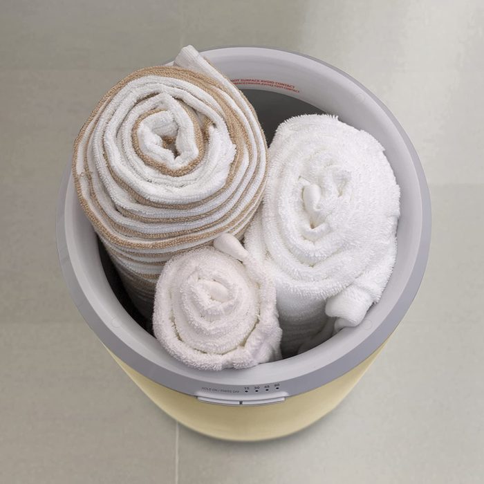 Rolled towels in various colors are stacked inside a round container, resting on a smooth, light-colored floor.