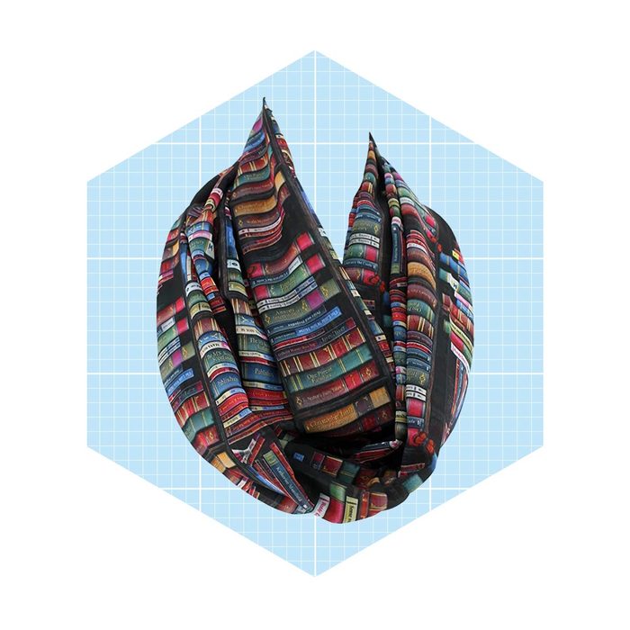 A scarf featuring a colorful design of stacked books is displayed in a stylized hexagonal outline against a light blue grid background.