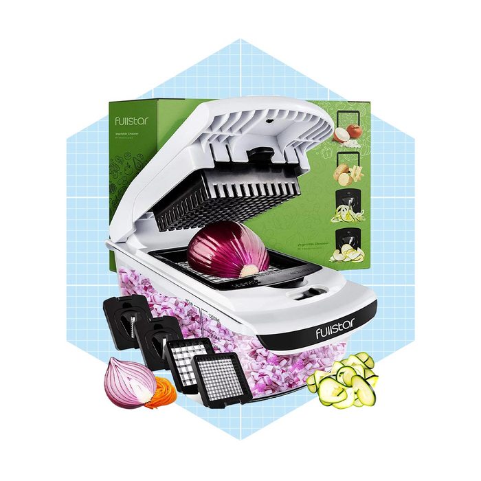 A vegetable chopper with an open lid is positioned over a red onion, surrounded by chopped vegetables and various cutting grids against a patterned background.