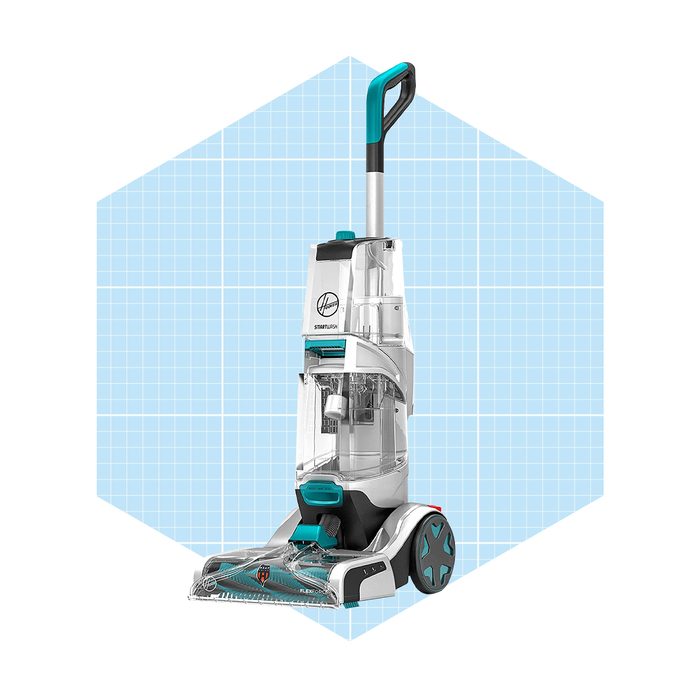 A carpet cleaner stands upright, ready for use, on a blue grid background, designed to deep clean surfaces while removing stains and dirt.