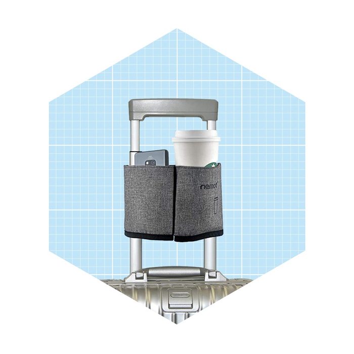 A travel suitcase handle features a gray fabric holder, displaying a phone and a coffee cup. The background is a light blue grid pattern.