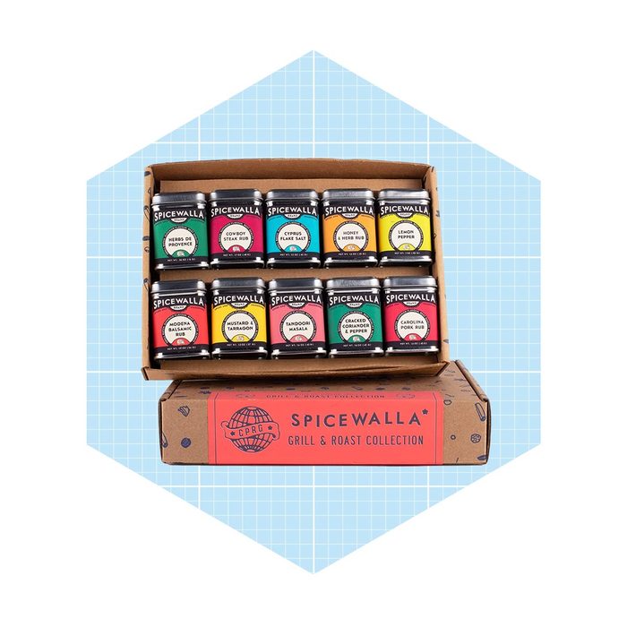 A collection of spice jars is arranged in a cardboard box. Labels feature various spice names, set against a light blue grid background.