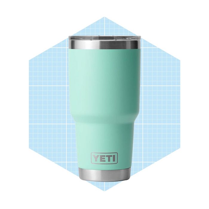 A turquoise insulated travel mug stands upright, featuring a stainless steel rim and a logo, against a light blue grid-patterned background.