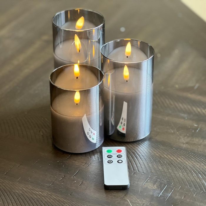 Three electric candles with flickering flames are placed on a wooden table, accompanied by a remote control resting nearby.