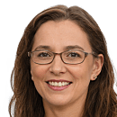 A woman with glasses smiles warmly, showcasing a friendly demeanor against a neutral background. Her hair is medium-length and slightly wavy.