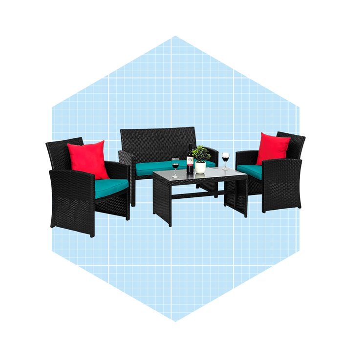 A black wicker seating set with bright cushions sits around a glass table, accompanied by drinks, against a light blue grid-patterned background.