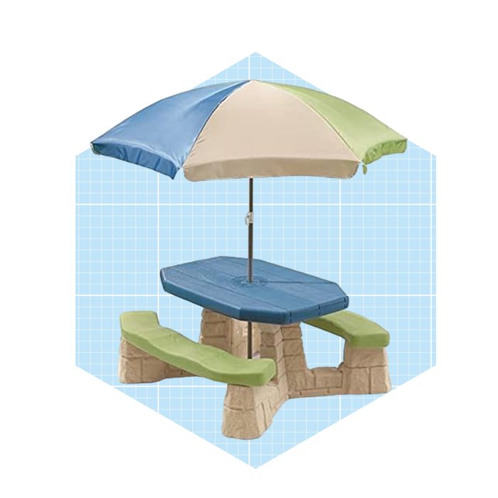 A child-sized picnic table with a colorful umbrella provides shade, situated in an undefined space with a light blue grid background.