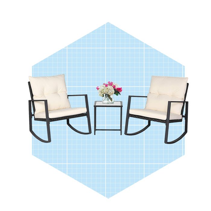 Two white cushioned rocking chairs are positioned beside a small table with a flower arrangement, set against a blue grid-patterned background.