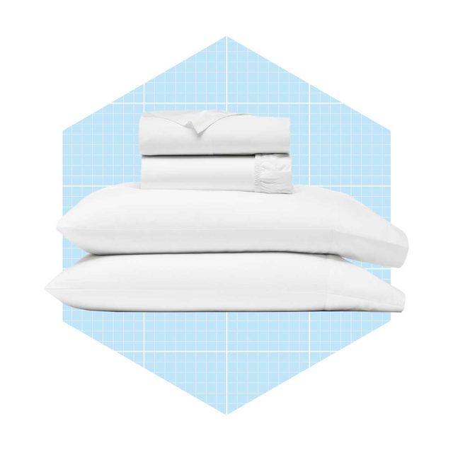 A stack of white bedding, including two pillows and a fitted sheet, rests against a light blue grid-patterned background.